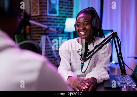 Une influenceur féminine interrogeant le client sur le flux de podcast, à l'aide de l'équipement d'enregistrement. Happy Woman diffuse un épisode en direct avec un homme en studio pour enregistrer une conversation pour la chaîne. Banque D'Images