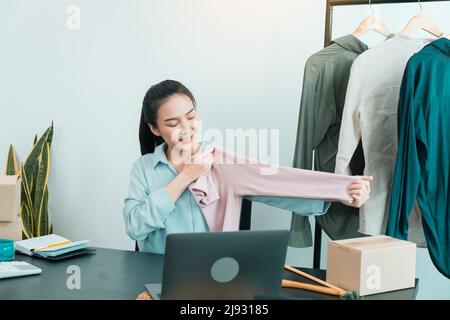 De jeunes entrepreneurs asiatiques ramassant des chemises pour comparer les proportions pour que les clients les voient en ligne. Banque D'Images