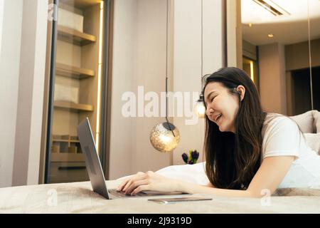 Femme asiatique posée sur son ordinateur portable tout en s'appréciant dans son lit dans sa chambre à la maison. Banque D'Images