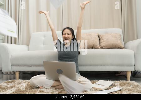 Une femme asiatique jette des papiers dans le salon alors qu'elle termine son travail avec son ordinateur portable sur ses genoux. Banque D'Images