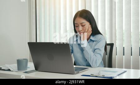 Les jeunes femmes asiatiques s'ennuient au travail et se sentent paresseuses de traiter les données sur leur ordinateur portable dans l'après-midi. Banque D'Images