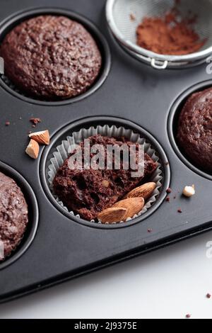 Muffins au chocolat fraîchement cuits dans une plaque de cuisson sur une table blanche avec des ingrédients Banque D'Images