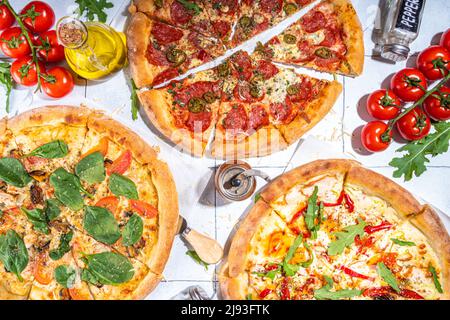 Trois pizzas variées, servies à la maison ou au restaurant sur une table carrelée avec des ingrédients de cuisine, tomate, basilic, épinards, pizza classique à l'arugula pepperoni Banque D'Images