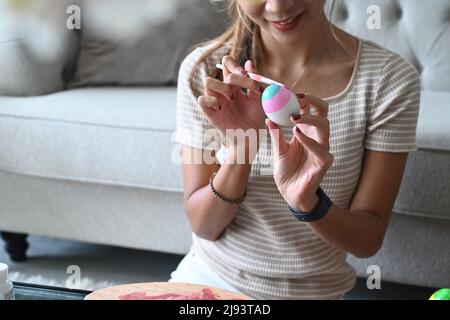 Jeune femme gaie assise sur le sol dans le salon et coloriage de l'oeuf pour le festival de Pâques. Banque D'Images