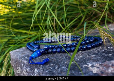 Perles de mala bleu ou perles de prière bouddhiste sur le rocher avec de l'herbe dans l'environnement naturel, gros plan et sélectif foyer. Accessoire de méditation Banque D'Images