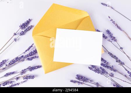 Une invitation blanche ou une carte de vœux avec de la lavande sur fond violet avec une enveloppe dorée. Modèle de carte Banque D'Images