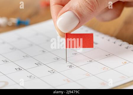 Les mains corrigeant l'horaire des notes, la vignette du drapeau rouge dans le calendrier pour la réunion et le rappel de rendez-vous Banque D'Images