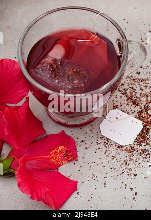 Thé hibiscus brillant et savoureux dans une tasse de verre, avec fleurs d'hibiscus et espace de copie Banque D'Images