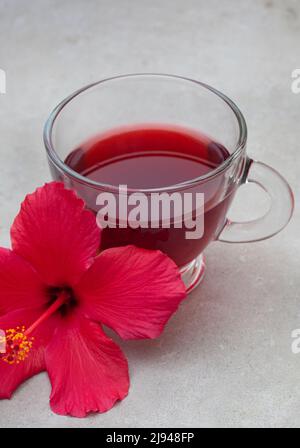 Thé hibiscus brillant et savoureux dans une tasse de verre, avec fleurs d'hibiscus et espace de copie Banque D'Images