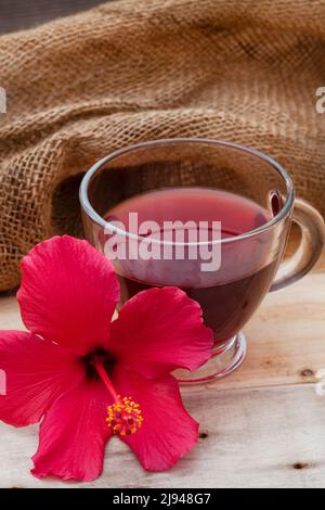 Thé hibiscus brillant et savoureux dans une tasse de verre, avec fleurs d'hibiscus et espace de copie Banque D'Images