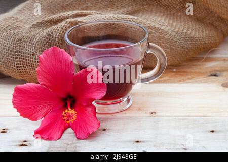 Thé hibiscus brillant et savoureux dans une tasse de verre, avec fleurs d'hibiscus et espace de copie Banque D'Images