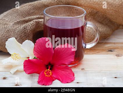 Thé hibiscus brillant et savoureux dans une tasse de verre, avec fleurs d'hibiscus et espace de copie Banque D'Images