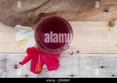 Thé hibiscus brillant et savoureux dans une tasse de verre, avec fleurs d'hibiscus et espace de copie Banque D'Images