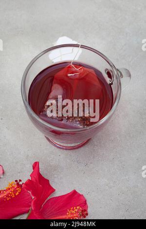 Thé hibiscus brillant et savoureux dans une tasse de verre, avec fleurs d'hibiscus et espace de copie Banque D'Images