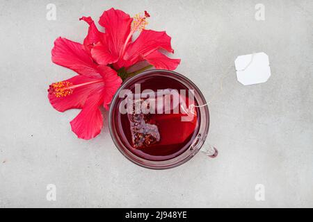 Thé hibiscus brillant et savoureux dans une tasse de verre, avec fleurs d'hibiscus et espace de copie Banque D'Images