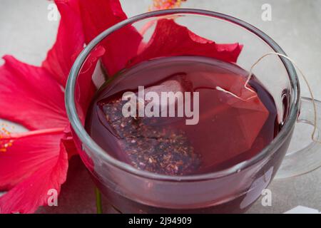 Thé hibiscus brillant et savoureux dans une tasse de verre, avec fleurs d'hibiscus et espace de copie Banque D'Images