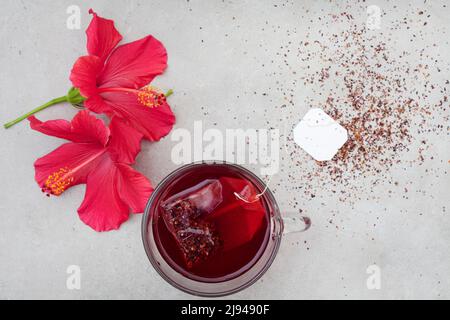 Thé hibiscus brillant et savoureux dans une tasse de verre, avec fleurs d'hibiscus et espace de copie Banque D'Images