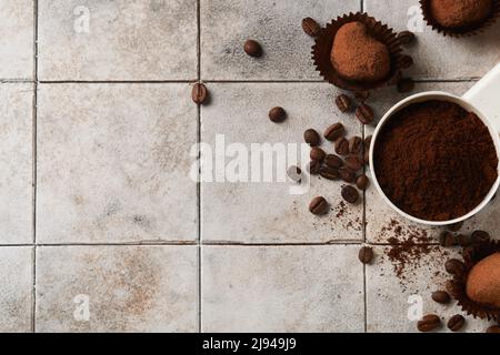 Fond de café. Cuillères à mesurer avec du café moulu, des haricots, une tasse et des truffes au chocolat doux sur un fond de table vieux carrelage fissuré. La nourriture. Banque D'Images