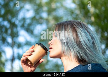 Une femme aux cheveux bleus prend un café à l'extérieur sur fond de nature. Banque D'Images