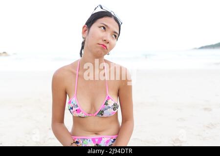Femme asiatique en maquillage et bikini avec expression de l'ennui sur la plage Banque D'Images