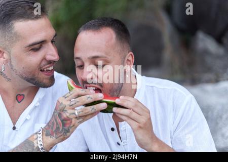 Gay homme se nourrissant de pastèque à son partenaire dans une plage Banque D'Images