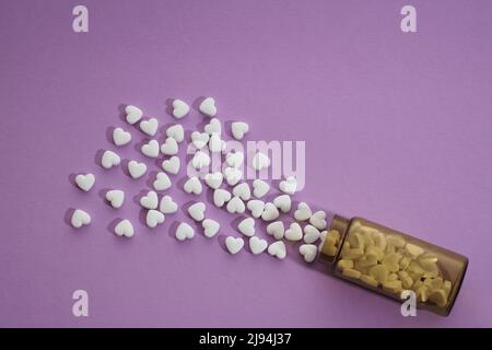 Vue de dessus de la bouteille de pilules déversées de forme de coeur sur fond violet Banque D'Images