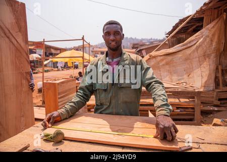 Carpenter dans un village africain prenant des mesures pour faire un morceau de mobilier. Banque D'Images