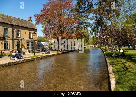 Les visiteurs apprécient une journée ensoleillée au printemps à Bourton-on-the-Water le long de la rivière Windrush, une destination populaire des Cotswolds, Gloucestershire, Angleterre, Royaume-Uni. Banque D'Images