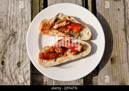 Deux tranches de pain avec sardines dans une sauce tomate sur une assiette blanche sur une table en bois par beau temps Banque D'Images