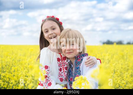 Joyeux garçon et fille 6-7 ans dans les vêtements nationaux ukrainiens parmi le champ de colza jaune en fleur. Jour de l'indépendance. Les enfants d'Ukraine sont demander Banque D'Images