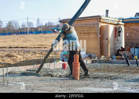 RÉGION DE LENINGRAD, RUSSIE - 28 MARS 2021 : un ouvrier invité à couler la fondation d'une maison de campagne l'après-midi de mars Banque D'Images