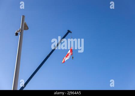 Photo conceptuelle montrant le drapeau canadien suspendu contre un ciel bleu avec une caméra de surveillance au premier plan, les citoyens étant confrontés à des restrictions plus strictes. Banque D'Images