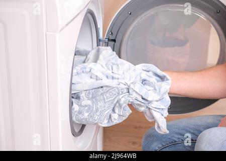 Un homme prend le linge de lit séché hors du sèche-linge. Sèche-linge dans la maison. Banque D'Images