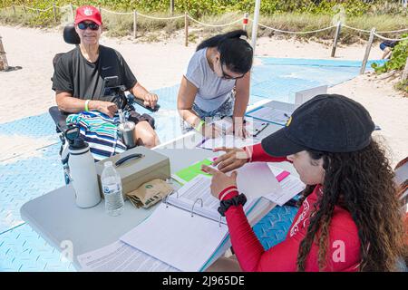 Miami Beach Florida, Sabrina Cohen Adaptive Beach Day, handicapés besoins spéciaux roues d'eau handicapées fauteuil roulant flottant, homme s'enregistrant Banque D'Images