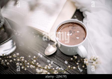 Tasse de cacao au chocolat chaud, vieux livre et fleurs de cerisier de printemps sur fond de bois. Concept de lecture Banque D'Images