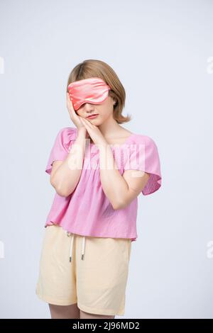 Portrait de jeune belle femme dormant avec masque oculaire sur fond blanc. Banque D'Images