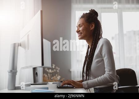 Portrait d'une jeune femme souriante et gaie qui travaille à partir de la navigation à domicile sur un ordinateur Banque D'Images