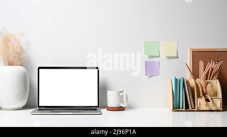 Ordinateur portable Mockup avec écran vierge, pot de fleurs, tasse à café et papeterie sur table blanche. Bureau à la maison Banque D'Images