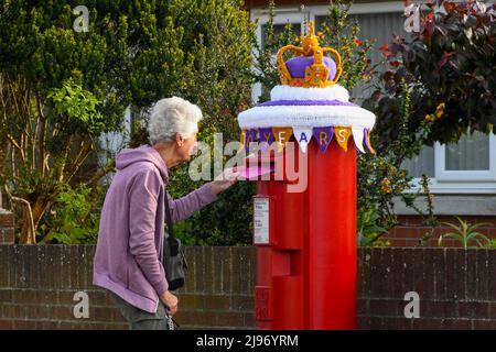 Weymouth, Dorset, Royaume-Uni. 21st mai 2022. Un résident affiche une lettre dans une boîte postale à Weymouth dans le Dorset, qui a été décorée d’une couronne d’État en crochet pour célébrer le Jubilé de platine de la Reine. Le Jubilé de platine d'Elizabeth II est célébré du 2 au 5 juin 2022 au Royaume-Uni et dans le Commonwealth pour marquer le 70th anniversaire de l'accession de la reine Elizabeth II le 6 février 1952. Crédit photo : Graham Hunt/Alamy Live News Banque D'Images