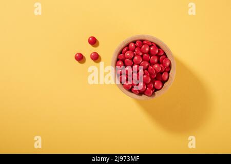 Pilules de bonbons au chocolat rouge dans un bol sur fond jaune Banque D'Images