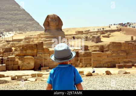 Giza, Egypte, juin 27 2017 : enfant touristique dans le plateau de Giza sur la rive ouest du Nil face à un Sphinx flou et aux pyramides de l'ancien W Banque D'Images