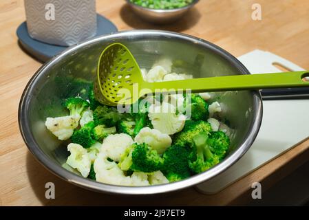 Brocoli et chou-fleur cuits à la vapeur dans un bol en métal avec une louche en plastique à trous Banque D'Images