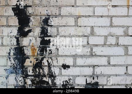Vieux mur de briques avec des éclaboussures de peinture noire. Banque D'Images