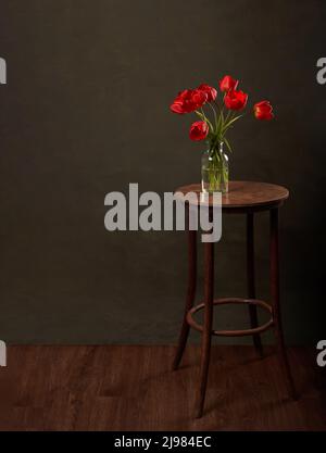 Vase avec fleurs sur table en bois. Table ronde avec tulipes rouges sur fond vert foncé avec espace de copie. Banque D'Images