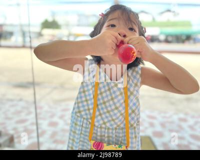 mignonne petite fille essaie de gonfler un ballon Banque D'Images