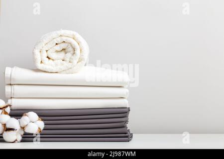 Une pile de draps gris et blancs, des draps et une serviette en rouleau pliée avec une branche de coton sur la table. Banque D'Images