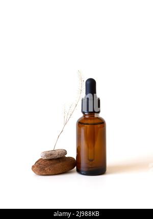 Bouteille en verre avec de l'huile aromatique ou du sérum de visage près des pierres et une petite branche d'herbe sèche. Concept cosmétique naturel bio spa. Vue avant. Fond blanc Banque D'Images