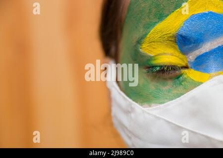 Enfant avec un masque avec son visage peint avec le drapeau du Brésil. Banque D'Images