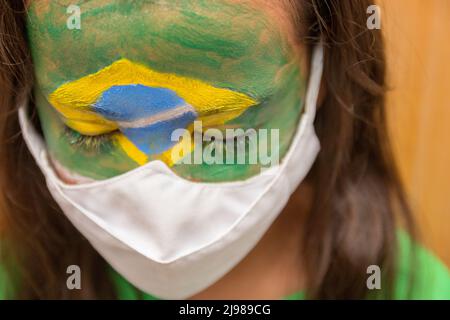 Enfant avec un masque avec son visage peint avec le drapeau du Brésil. Banque D'Images