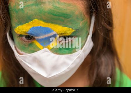 Enfant avec un masque avec son visage peint avec le drapeau du Brésil. Banque D'Images